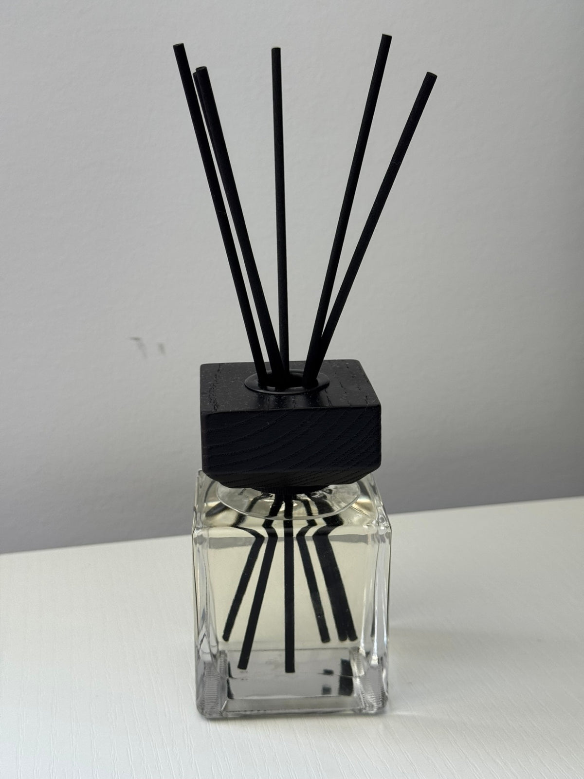 Veluno reed diffuser — clear square glass bottle with a black wooden cap and black reeds